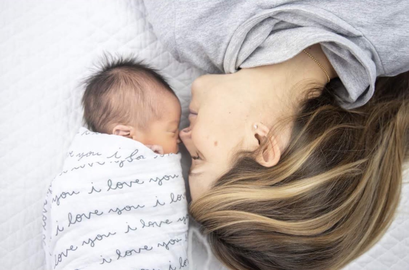 Mamá acostada frente a frente con su bebé envuelto en una manta